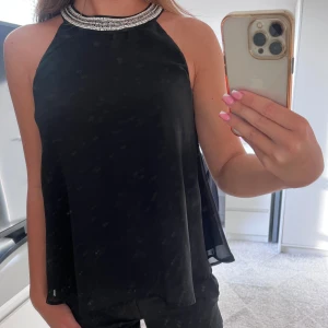 Svart halterblus - Säljer en super snygg svart halterblus från Vero Moda i storlek S. Blusen har en elegant design med strasshalsband som ger en extra touch. Den är i utmärkt skick och kan kombineras med både byxor och kjolar för en komplett look!