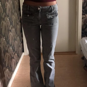 Grå jeans med låg midja - Säljer ett par grå jeans med låg midja. De har en straight passform och är i en klassisk jeansstil med knappar och fickor fram. 
