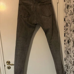 Grå jeans från Dressmann - Säljer ett par grå jeans från Dressmann i storlek 30/32. De har en slim passform och är perfekta för både vardag och fest. Jeansen har en klassisk design med fem fickor och knappar i midjan. De är i bra skick och redo för en ny ägare!