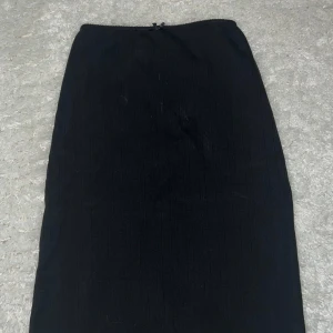 Svart kjol från BikBok - Säljer en stilren svart kjol från BikBok i storlek XS. Kjolen har en enkel design med en liten rosett som detalj i midjan matchar perfekt till den svarta toppen🙌