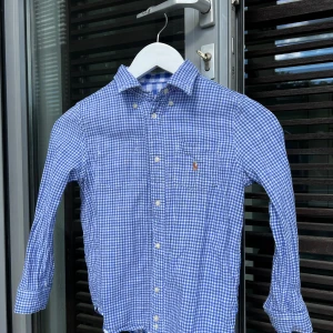 Ralph Lauren Skjorta, Vändbar barn 5-6 -  Superfin vändbar Ralph Lauren skjorta i storlek  5-6 år köpt på Mehls Östermalm. Små rutig på ena sidan och stor rutig på andra sidan. Den klassiska hästen i många färger på båda sidorna. 
