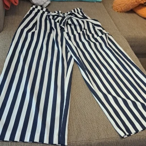 Randiga byxor med knytband - Säljer ett par supertrendiga randiga byxor i blått och vitt. De har en loose fit och är högmidjade med ett snyggt knytband i midjan. Perfekta för både vardag och fest! 🥳
