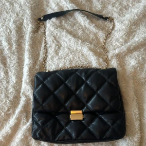 Svart väska - En rymlig svart väska med guldfärgad kedja och knippe. 