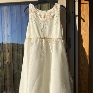 Vit klänning från Monsoon - Säljer en superfin vit klänning från Monsoon i storlek 12-13 år. Klänningen är ärmlös och har vackra blommiga detaljer på överdelen. Den har en elegant och luftig kjol som ger en drömlik känsla. Perfekt för sommarens fester eller speciella tillfällen! 🌸 Använd endast en gång då de var för ett bröllop! Nypris 1200kr
