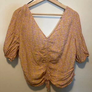 Blommig topp - Blommig v-ringad topp. Endast använd 1 gång. Ärmarna är tre-kvarts-längd med resår vid ärmsluten