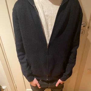Mörkblå stickad hoodie - Säljer en mörkblå stickad hoodie med dragkedja. Har knappt används då den var för liten. Den har väldigt bra passform. 