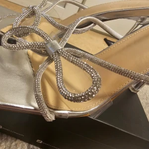 Silvriga sandaler med glittrig rosett - Snygga silvriga sandaler med en glittrig rosett på ovansidan. 39 men passar även 38, aldrig använt 