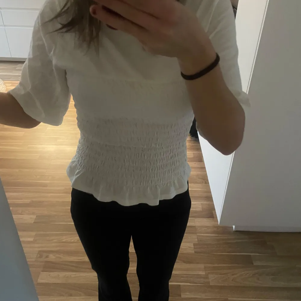 Säljer en superfin vit smockad topp med trekvartsärm. Den har en söt volangdetalj vid nederkanten och är perfekt för både vardag och fest. Toppen är i mycket bra skick och passar perfekt till jeans eller kjol. Perfekt för vår och sommar!. Yläosat.