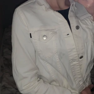 Vit jeansjacka - Säljer en vit jeansjacka i bra skick. Den har knappar framtill och två bröstfickor med lock. Jackan har en normal passform och långa ärmar.