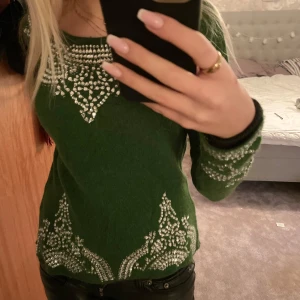 Grön tröja med strassdetaljer från Day Birger & Mikkelsen - Säljer en superfin grön tröja från Day Birger & Mikkelsen i storlek S. Tröjan har långa ärmar och är dekorerad med vitt strass i ett snyggt mönster. Perfekt för höst och vinter, både mysig och stilren. 