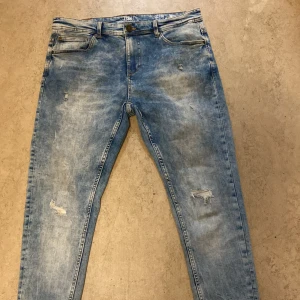 Blå jeans med slitningar - Säljer ett par snygga blå jeans  i storlek 32/30. De har en cool slitningseffekt och en klassisk femficksdesign, de är i slim fit, Det är bara att hojta till vid någon fundering