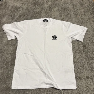 Vit t-shirt från Dsquared2 - Säljer en snygg vit t-shirt från Dsquared2 i storlek 14Y. Den har en stilren design med ett svart lönnlöv och text på bröstet. Perfekt för en casual look eller att styla upp med en jacka. T-shirten är i bra skick och gjord av mjuk bomull. Passar perfekt till sommaren! 🌟köpt på kids brand store
