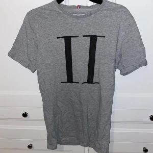 Grå t-shirt från Les Deux - Snygg grå t-shirt från Les Deux med ett stilrent svart tryck på framsidan. Perfekt för en avslappnad look. Tillverkad i mjukt material för extra komfort.