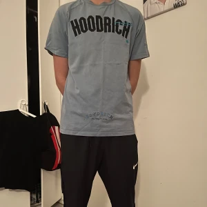 Blå t-shirt från Hoodrich - Säljer en blå t-shirt från Hoodrich med tryck både fram och bak. T-shirten har korta ärmar och en avslappnad passform. Perfekt för en casual look.