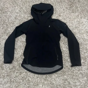 Peak Performance jacka - Snygg svart jacka från Peak Performance med huva och dragkedja. Perfekt för utomhusaktiviteter med sin stilrena design och funktionella detaljer.