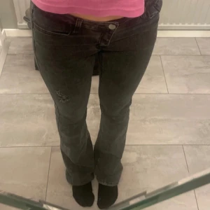 Svarta jeans - Säljer ett par svarta jeans i bra skick med coola slitningar på ena benet. De har en tight passform och är lågmidjade, vilket ger en snygg siluett. Perfekta för både vardag och fest! 🖤 OBS!: en av bälteshällorna är sönder!
