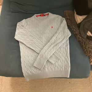 Morris tröja - Säljer en stilren ljusgrå stickad tröja från Morris i 100% merinoull. Tröjan har ett snyggt kabelstickat mönster och en röd broderad detalj på bröstet. Perfekt för både höst och vinter, och den är supermjuk och varm. Priset är inte hugget i sten. Rensar garderoben kan köpas för 350 vid snabb affär 