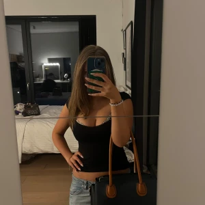 Svart handväska med bruna detaljer - Snygg svart handväska i mycket bra skick med bruna handtag och detaljer. Perfekt för både vardag och fest. Väskan har en stilren design och är rymlig nog för alla dina nödvändigheter. En klassisk accessoar som passar till alla outfits!