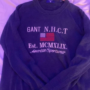 Mörkblå tröja från Gant - Säljer en snygg mörkblå tröja från Gant med broderad text och amerikansk flagga på framsidan. Tröjan har en ribbad krage och är perfekt för en casual look. Passar bra till jeans eller chinos.