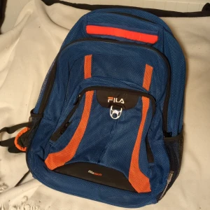 Blå limited edition ryggsäck från Fila i tätt nät - Snygg blå ryggsäck från Fila med orange detaljer och flera praktiska fack. Perfekt för skolan eller träningen. Justerbara axelremmar för extra komfort och en robust dragkedja för säker förvaring.