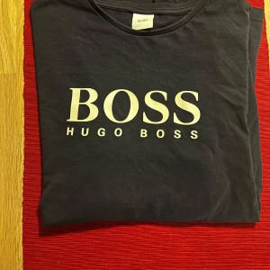 Mörkblå  långärmad tröja från Hugo Boss - Snygg svart långärmad tröja från Hugo Boss med vit logotyp på bröstet. Perfekt för en stilren och avslappnad look.Tyvärr står det ingen strl, men typ xs eller ungdom kanske strl 160-170.