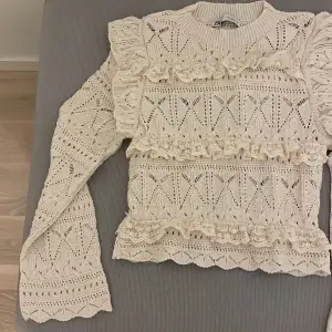 Säljer en superfin beige stickad tröja från Zara. Den har ett vackert spetsmönster och volangdetaljer som ger en fin touch. Perfekt för höst och vår! Tröjan har långa ärmar och en normal passform. Passar både till vardags och fest. 