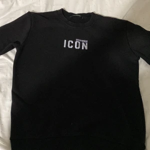 Svart sweatshirt från Dsquared2 - Säljer en svart sweatshirt från Dsquared2 i storlek M. Tröjan har texten 'ICON' tryckt på framsidan och är i mycket bra skick. Perfekt för en stilren och avslappnad look. Passar bra till både vardag och fest!