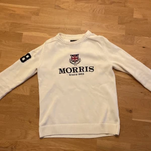 Vit tröja från Morris - Säljer en stilren vit tröja från Morris med ett tryck av brittiska flaggan och texten 'Morris Since 1968' på framsidan. Tröjan har långa ärmar med siffran '68' tryckt på ena ärmen. Perfekt för en casual look.