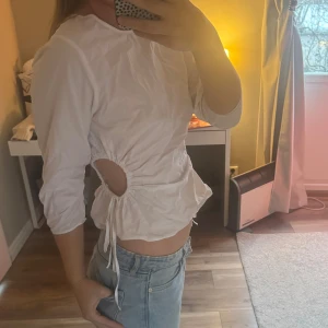 Vit topp med knytning i sidan - Säljer en snygg vit topp med trekvartsärm och coola knytningar i sidan. Cutout i sidorna. Köpt på Zara knappt använd!