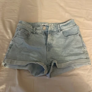 Ljusblå jeansshorts från Superdry - Säljer ett par ljusblå jeansshorts. De har en klassisk femficksdesign med upprullade benslut och knappgylf. Perfekta för sommardagar!