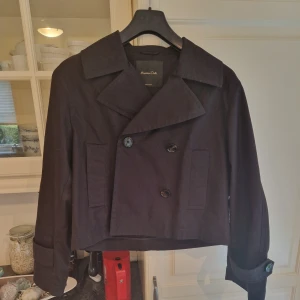 Brun kort kappa från Massimo Dutti - Snygg och trendig kappa från Massimo Dutti med dubbelknäppning och bred krage. Jackan är croppad och har långa ärmar med knappar vid ärmsluten. Perfekt för en stilren look. Använd fåtal gånger, inga defekter, nyskick. 
