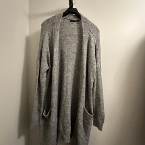 Grå stickad kofta - Mysig grå kofta från Lager 157 i storlek M/L som är oanvänd. Perfekt för kyliga dagar med sina långa ärmar och praktiska fickor framtill och mysig material.