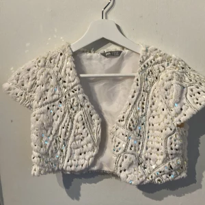 Vit paljettprydd bolerotopp från Lindex - Säljer en superfin vit bolerotopp från Lindex Kids. Den är täckt med glittrande paljetter. Perfekt för festliga tillfällen! Toppen är kortärmad och har en öppen design framtill.