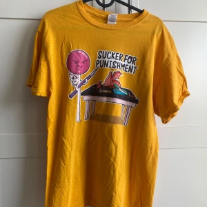 Gul t-shirt med tryck - Säljer en cool gul t-shirt med ett roligt tryck av en klubba och texten 'Sucker for Punishment'. Använd nån gång.