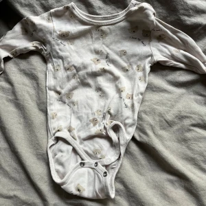 Vit långärmad body från H&M - Säljer en söt vit långärmad body från H&M i ekologisk bomull. Den har ett gulligt mönster med små björnar och texten 'I love my family'. Perfekt för de minsta att mysa i! 💕