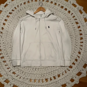 Vit hoodie från Polo Ralph Lauren - Säljer en stilren vit hoodie från Polo Ralph Lauren. Den har en dragkedja framtill och en klassisk logga på bröstet. Perfekt för både vardag och i skolan. Den är i bra skick och supermjuk att ha nu till höst och vinter, storleken är S