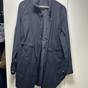Svart kappa med knappar - Säljer en stilren svart kappa i bra skick. Den har långa ärmar och knappar framtill. Perfekt för höst och vår, med en klassisk design som passar till det mesta. Storleken är normal och materialet känns slitstarkt och bekvämt.