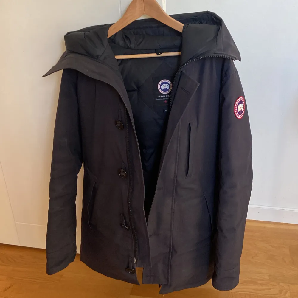 Säljer en svart Canada Goose vinterjacka i mycket bra skick. Jackan har en klassisk design med dragkedja och knappar, samt en varm huva. Perfekt för kalla vinterdagar. Den är både stilren och funktionell, vilket gör den till ett måste i garderoben. Passar perfekt för vinterns alla äventyr! ❄️. Jackor.