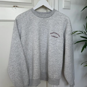 Grå sweatshirt från Gina Tricot - Säljer en snygg grå sweatshirt från Gina Tricot med texten 'San Francisco California' tryckt på bröstet. Tröjan är i helt nytt skick. Perfekt för höst och vår! 
