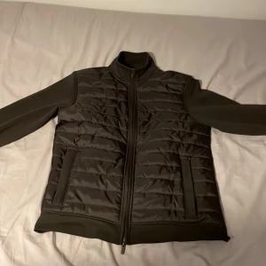 Svart quiltad cardigan jacka från Dressmann - Säljer en svart quiltad jacka från Dressmann i storlek M. Jackan har en dragkedja framtill och är perfekt för höst och vår. Den är i mycket bra skick och har en stilren design med långa ärmar. Perfekt för en casual look eller en promenad i stan.