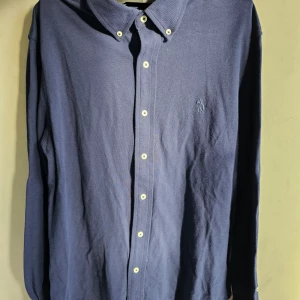 Ralph lauren mörkblå skjorta - Säljer en RALPH LAUREN  mörkblå skjorta med klassisk krage och knappar hela vägen ner. Skjortan har en broderad logga på bröstet och är perfekt för både vardag och fest. Materialet känns mjukt och bekvämt, vilket gör den idealisk för höst och vår. Passar bra till jeans eller chinos för en avslappnad men ändå uppklädd look.