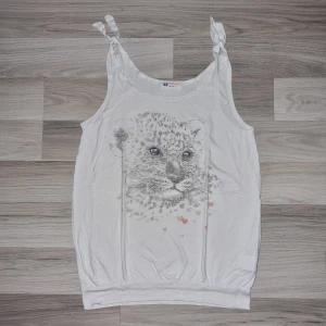 Vit linne med leopardtryck från H&M - Säljer ett supergulligt vitt linne från H&M med ett leopardtryck på framsidan. Linnet har knytband på axlarna och är perfekt för sommardagar. Den har ett litet hål på vänster framsida, annars i bra skick 🐆✨