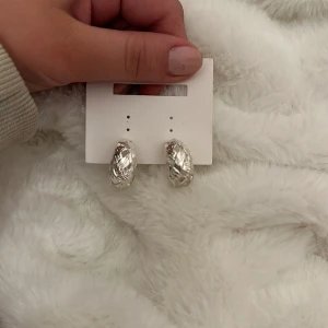 Silverfärgade örhängen med mönster - Säljer ett par snygga silverfärgade örhängen med ett unikt mönster. De är i mycket bra skick och perfekta för att ge en extra touch till din outfit. Passar både till vardag och fest!