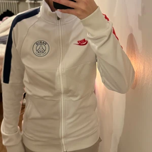 Nike/Psg jacka - Säljer en snygg vit Nike jacka med PSG-logga på bröstet. Xs men sitter som s. Unisex. Nypris 1100kr!