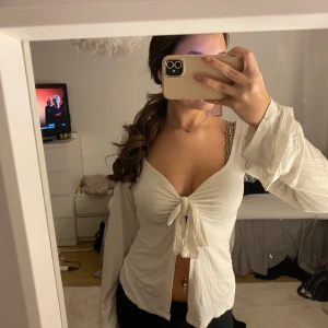 Vit långärmad topp med knyt - Säljer en superfin vit långärmad topp med knyt framtill. Den har en djup v-ringning och är perfekt för både vardag och fest. Materialet är mjukt och bekvämt, vilket gör den idealisk för vår och sommar. Passar perfekt med jeans eller kjol för en chic look!