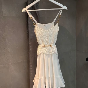 Ida Sjöstedt-klänning med volanger och spetsdetaljer - Säljer en superfin vit klänning med spetsdetaljer och volanger. Den har smala axelband och ett bälte i midjan för en snygg passform. Perfekt för sommarens fester, student eller midsommarfirandet! 💃