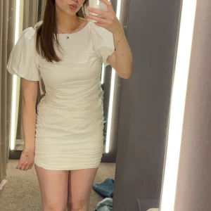 Vit kortklänning med puffärmar - Säljer en superfin vit kortklänning med puffiga kortärmar och en smickrande tight passform. Klänningen har en elegant öppen rygg och är perfekt för studenten.