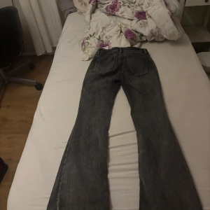 Grå jeans med bootcut - Säljer ett par grå jeans i bootcut-stil. De har en sliten look vid fållen, vilket ger dem en cool vintage-känsla. Perfekta för en avslappnad vardagsstil. Passar bra till sneakers eller boots.
