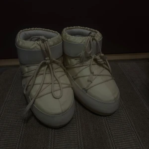 Vita moon boots med snörning - Säljer ett par vita moon boots i syntetmaterial. De har en cool och chunky design med snörning framtill. Perfekta för vinterns kalla dagar och håller fötterna varma och torra. Passar både till vardags och snöiga äventyr!