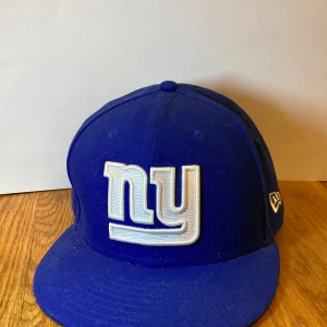 Blå New York keps från New Era - Säljer en blå keps från New Era med broderad NFL-logga och 'ny' på framsidan. Kepsen är i bra skick och perfekt för sportfantaster. Den är gjord av polyester och har en klassisk passform.